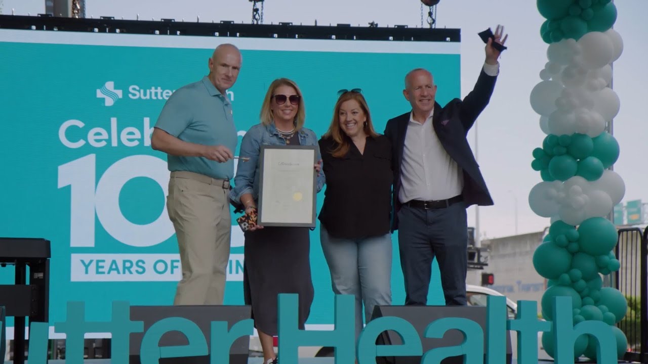 Three individuals proudly displaying a certificate on a stage.