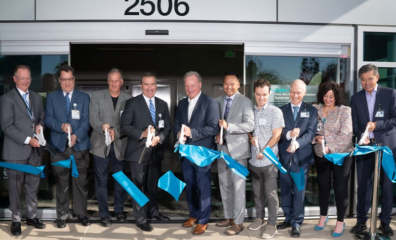 Group of people cutting blue ribbon at business grand opening.